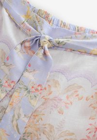 Doorzichtige bloemenrokstof met een pastelpaars tailleband dat in een strik is gebonden, met roze, gele en groene botanische printdetails.