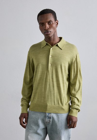 Camisa polo de manga larga verde claro con cuello abotonado, que presenta una tela texturizada y puños acanalados, combinada con jeans de denim claros.