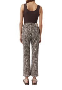 Braunes Tanktop kombiniert mit hochgeschnittenen, geraden Hosen mit einem Leopardenmuster in Braun und Creme, dazu flache Sandalen und ein Taillendetail.