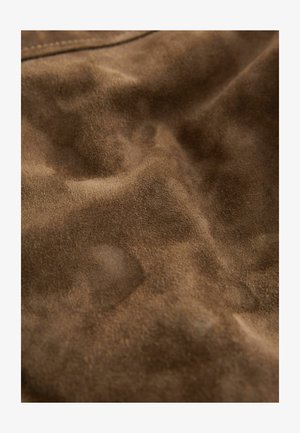 Brunt ruskindsmateriale med en blød, struktureret overflade, der viser subtile variationer og lysrefleksioner. Ingen tydelige mønstre eller metaldele synlige.