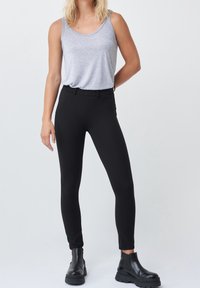 Černé skinny kalhoty s hladkým povrchem a elastickým pasem, spárované s šedým bezrukávovým topem a černými kotníkovými botami.