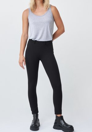 Svarta smala byxor med en slät yta och elastisk midja, kombinerade med en grå ärmlös topp och svarta ankelsemlor.