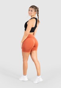 Zwarte cropped tanktop en oranje high-waisted shorts. De stof lijkt glad met een aangesloten ontwerp. Witte sneakers maken de uitstraling compleet.