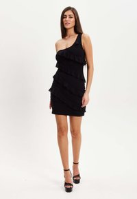 Black one-shoulder dress with layered ruffles, fitted silhouette, and short length. Paired with black platform heels.