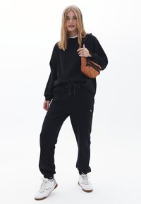 Felpa nera con una vestibilità comoda, abbinata a joggers neri con vita elastica. Borsa a tracolla trapuntata marrone e sneakers bianche.