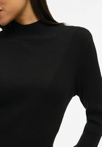 Maglione aderente nero a collo alto in maglia ribbed presenta motivi testurizzati diagonali, una forma attillata e una finitura liscia. Adatto per essere indossato a strati o come capo indipendente.