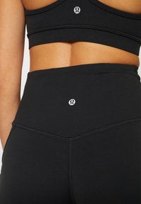 Musta korkeavyötäröinen leggari joustavaa kangasta, jossa on teksturoidun muotoilu ja pieni logo-yksityiskohta vyötäröllä.