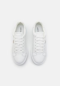 Zapatillas blancas de cuero con parte superior texturizada, punta redonda, cordones planos y suela de goma blanca. Presentan un logotipo en el lateral.