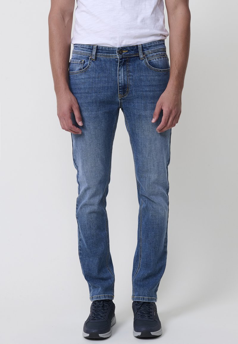 Modre jeans iz denima s ravno nogavico, petimi žepi in svetlim zbledeljem na sprednji strani, z rumenimi šivi in klasičnim gumbom za zapiranje.