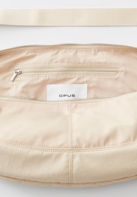 Borsa a spalla beige realizzata in un tessuto in nylon liscio, con scomparto principale con zip, tasca interna e etichetta con logo. Presenta una larga tracolla intrecciata.
