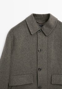 Cappotto in misto lana di colore grigio scuro, con colletto, bottoni frontali, due tasche a toppa e una finitura testurizzata.