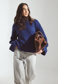 Navy blue knitted sweater with ribbed cuffs, paired with light gray wide-leg jeans and a brown suede handbag.