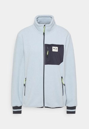 Veste polaire bleu clair avec une poche poitrine zippée noire, fermeture éclair frontale complète, deux poches latérales zippées et des poignets noirs avec bandes réfléchissantes.