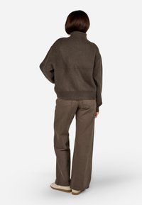 Ruda, per didelį dydį megzta suknelė su aukštu kaklu ir raukšlėtu apačiu; derinama su šviesiai rudomis plačiomis kelnėmis ir šviesių spalvų avalyne.