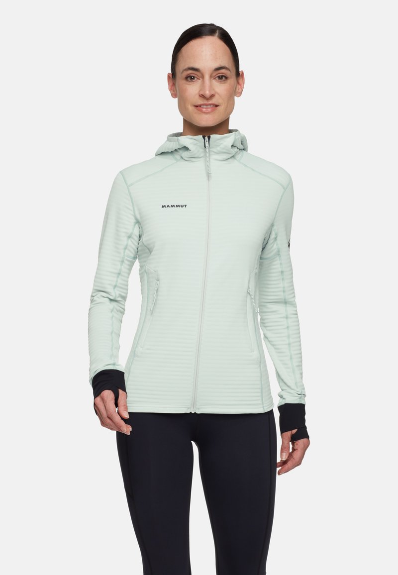 Giacca con cappuccio verde menta chiaro con zip frontale, trama a coste, dettagli neri sui polsini e tasche laterali. Adatta per attività all'aperto.