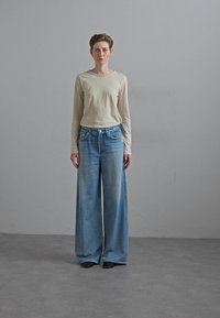 Light beige long-sleeve shirt paired with wide-leg, faded blue denim jeans. The outfit features a relaxed fit and subtle texture.