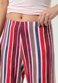 Pantalons larges multicolores avec un motif à rayures verticales en rouge, rose, violet et marron. Tissu doux et ceinture élastique.