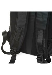 Mochila negra con correas acolchadas, con herrajes de hebilla ajustables y una textura de nailon suave, que exhibe un diseño elegante y minimalista.