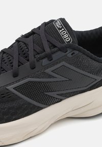Baskets de course noires avec une tige en maille texturée, semelle en caoutchouc et lacets. Détails notables : un logo sur la languette et des accents sur les côtés.
