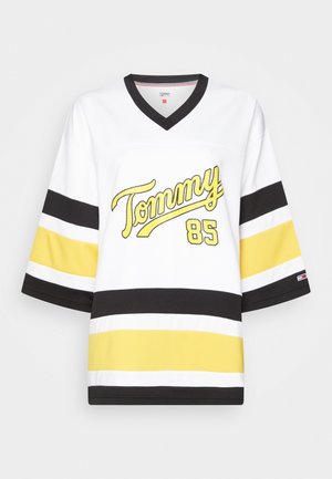 Biały hockey styl koszulka z czarnymi i żółtymi paskami, napisem "Tommy" i numerem 85 w żółtym na przodzie, czarnym kołnierzem w kształcie litery V.
