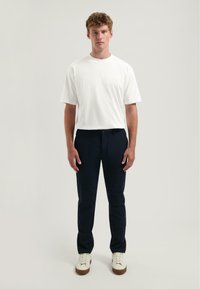 Wit T-shirt met korte mouwen, marineblauwe broek en witte sneakers met een bruine zool. Eenvoudig ontwerp, rechte pasvorm, de stof heeft een gladde textuur.