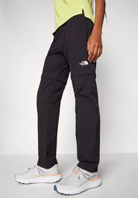 Černé nákladní kalhoty s odnímatelnými nohavicemi na zip, vyrobené z lehké látky. Mají logo The North Face na stehně a praktické kapsy.