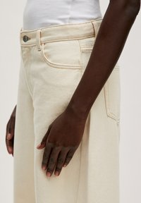 Crème-kleurige wijde jeans met een lichte textuur, voorzien van licht stiksel, voorzakken en een knoopsluiting bij de taille.