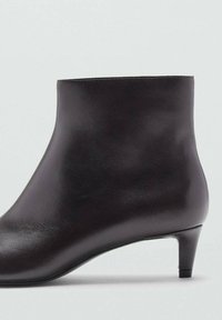 Bottines en cuir noir avec une texture lisse et épurée, une silhouette effilée et un petit talon, conçues pour un look minimaliste.