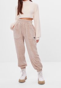 Beige fleece joggers met elastische tailleband, zijzakken en geribbelde boorden; gecombineerd met een lichte cropped trui.