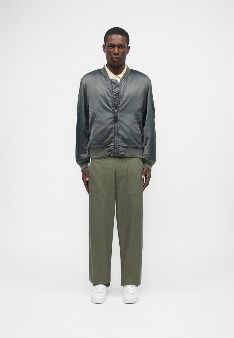 Jachetă bomber pentru bărbați din satin gri închis cu față matlasată, combinată cu pantaloni largi de culoare verde măsliniu și adidași albi.