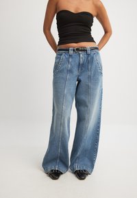 Širši traper hlače v svetlo modri barvi z izbledelim izgledom, z visokim pasom, zankami za pas in dvema sprednjima žepoma.