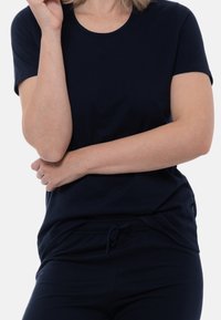 T-paita tummansinisestä puuvillasta, jossa on lyhyet hihat, pyöreä kaula-aukko ja rento malli. Yhdistetty yhteensopivien naruhousujen kanssa.