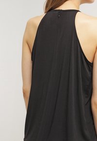 Top nero senza maniche con vestibilità ampia, dotato di scollatura alta e zip esposta sul retro, realizzato in tessuto morbido e liscio.