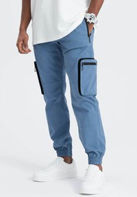 Pantalons cargo bleu clair avec poignets élastiques, dotés de deux poches latérales et d'une poche zippée sur la cuisse, fabriqués à partir d'un tissu résistant.
