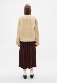 Casaco bege de pele falsa com mangas compridas, combinado com uma saia midi plissada castanho escuro. Textura suave, costuras mínimas e sem fechos visíveis.