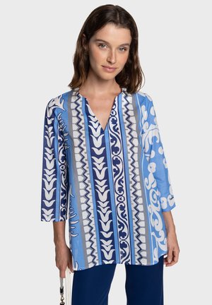 Blusa azul con estampado y mangas tres cuartos, que presenta franjas alternas en tonos más claros y oscuros de azul y diseños decorativos blancos.