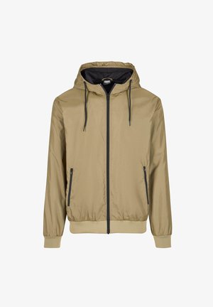 Giacca a zip con cappuccio color tan e interno nero. Caratterizzata da lacci regolabili, due tasche frontali e polsini e orlo a coste. Leggera, con una texture liscia.