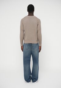 Jasnobrązowy prążkowany sweter w połączeniu z luźnymi niebieskimi jeansami z tylną kieszenią. Gładka faktura, luźny krój.