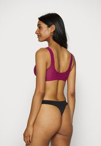 Magenta blondebralette med bølgede kanter og brede stropper, parret med en sort trusse. Glatt tekstur, feminin design og tettsittende form.