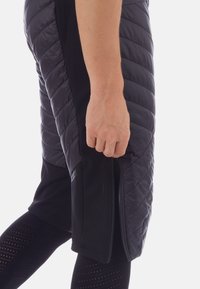 Pantaloni corti imbottiti neri con una texture trapuntata e una cerniera laterale. Il tessuto ha una finitura liscia, in contrasto con leggins in rete traspirante.