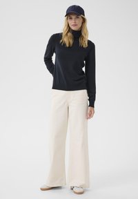 Navy turtleneck sweater paired with cream wide-leg pants, featuring a relaxed fit. A navy cap completes the outfit, worn with white shoes.