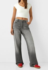 Breda grå jeans med en urtvättad textur, med knäppning och bältesöglor. Matchat med en vit crop top och röda sneakers.