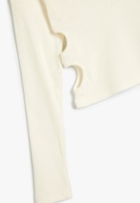 Rippenteil mit langen Ärmeln in Off-White, das ein einzigartiges Ausschnittdetail auf der linken Seite und ein weiches, flexibles Material aufweist.