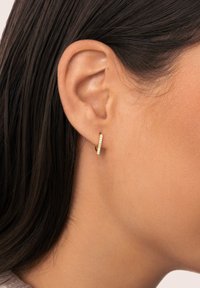 Boucle d'oreille en or en forme d'anneau avec une bande droite ornée d'une rangée de petites pierres transparentes le long du bord avant, mettant en valeur une texture lisse et polie.