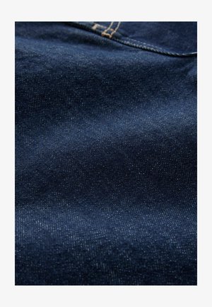 Denimová látka v tmavě námořnické modři, s hladkou strukturou a jemným leskem, vykazující svislé tkané vzory a kontrastní švy.