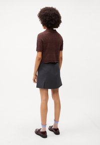 Καφέ πλεκτό τοπ κοντομάνικο με κολάρο, συνδυασμένο με σκοτεινό γκρι μίνι φούστα που έχει σχισμή στο πίσω μέρος και καφέ παπούτσια με κάλτσες σε μπλε απόχρωση.