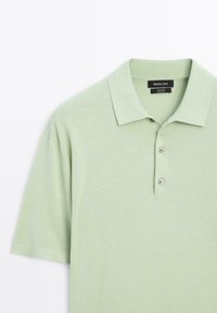 Polo in cotone verde chiaro con una texture liscia, maniche corte e un colletto a due bottoni. Caratterizzato da un colletto pieghevole e orlo cucito.