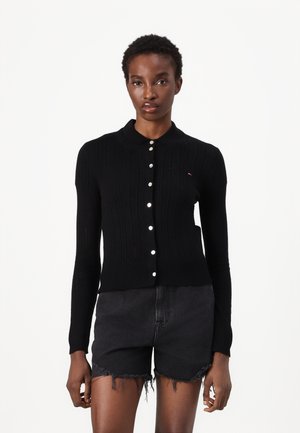 Cardigan noir avec un design en tricot texturé, col côtelé et fermeture à boutons. Présente des boutons ivoire et un logo minimal.