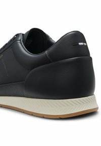 Baskets en cuir noir avec talon rembourré, semelle intermédiaire blanche à motif chevrons, et petit détail cousu en noir, blanc et beige à l'arrière.