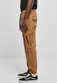 Khaki cargo kalhoty s mnoha kapsami, elastickými manžetami a šňůrkovým pasem. Vyrobené z tkaniny smíšené s bavlnou.